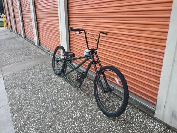 Long black chopper build leaning against the shop's orange roll-up door